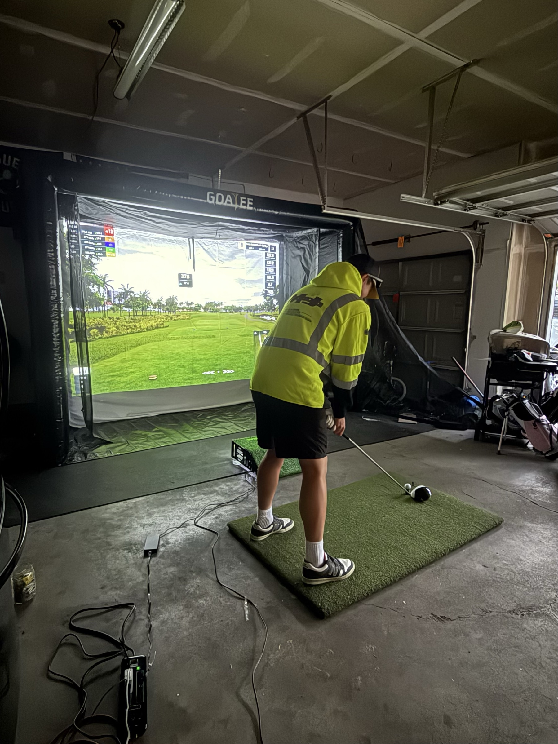 Golfer teeing up a driver on the hitting mat inside the Goatee bay, course projected on screen